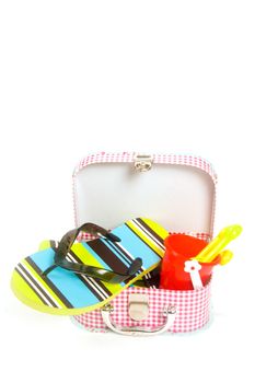 small suitcase with sand toys and green striped slippers on white