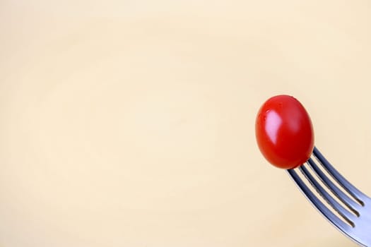 Single tomato on a fork against a yellow plate