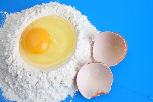 Raw egg in flower with egg shells, against a blue background