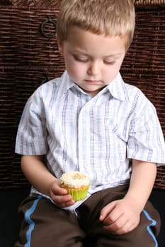 Beuatiful Blond toddler looking down at his cupcake