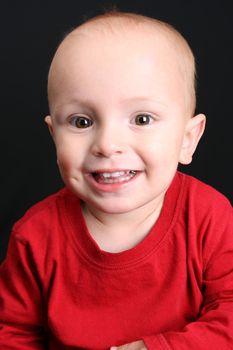 Blonde toddler against a black background with a big smile