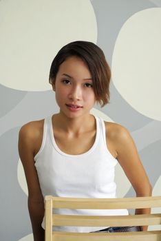 A young and sexy Asian woman sitting on a chair and posing in front of a grey bubble background. Adobe RGB color profile.