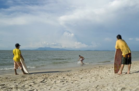A young man skin boarding at the beach while his friends look on. 