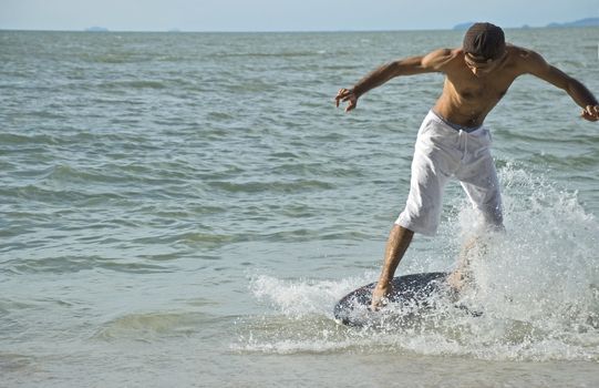 A young man skin boarding at the beach on a sunny day.