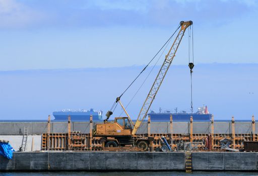 Mobile crane standing on the quay with two ships in background
