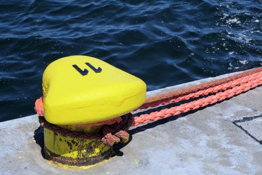 Yellow bollard mounted to the quay with ropes for mooring ships
