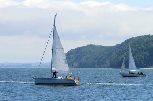 Two sailboats floating on the sea with cliffs in background
