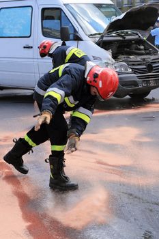 Fire fighters throwing the sand on the street with oil from smashed car
