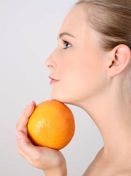 Beautiful young model holding an orange under her chin