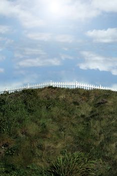 a white picket fence on top of a hill against a cloudy sky