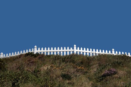 a white picket fence on top of a hill against a blue sky