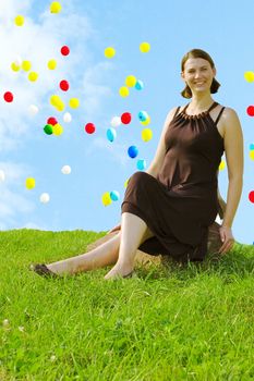 Smiling girl sitting on stone. Flying balloons on blue sky background.