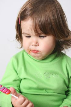 Toddler girl with chubby cheeks eating a sticky lollipop