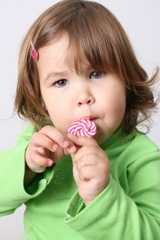 Cute brunette toddler eating lollipops wearing a green shirt