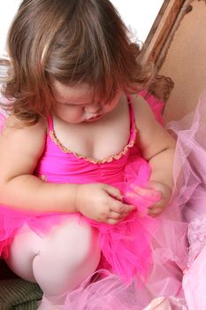 Little girl wearing a pink tutu, sitting inside an antique suitcase
