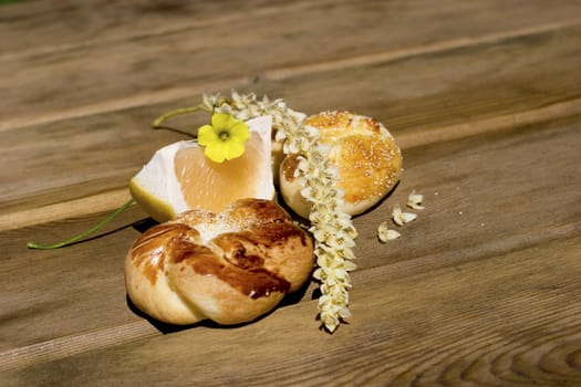 Segment of grapefruit with buns and flowers in wooden table.