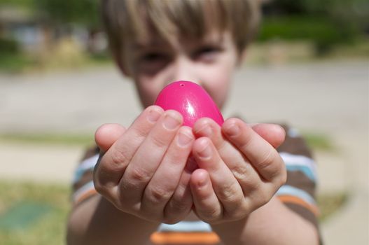 A small boy holds up a colorful, plastic easter egg.
