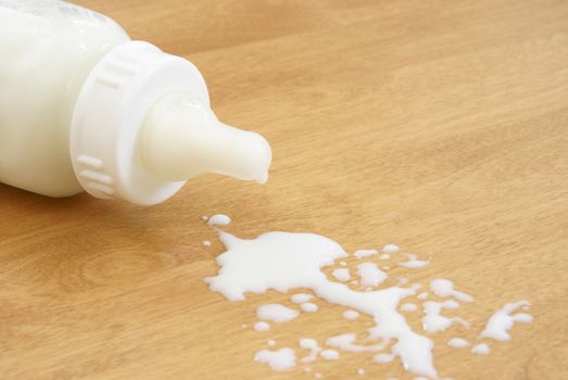A baby bottle has tipped over and milk has been spilled.