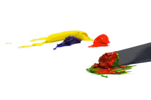 Yellow, blue, and red paint blobs being mixed by an artiists pallete knife