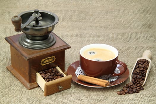 Delicious coffee with vintage coffee mill on brown background