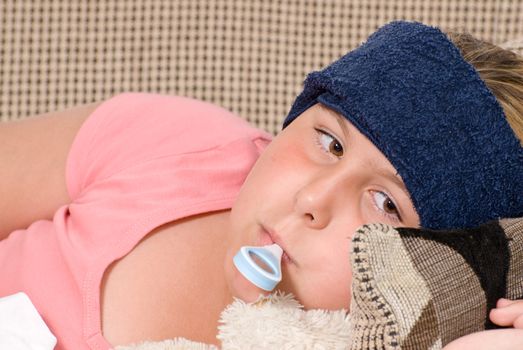 Closeup view of a young girl with a thermometer in her mouth and a damp cool cloth on her forehead, indicating she has a fever