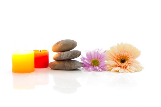 A spa theme still life with candle, river stones and flowers, isolated on white with reflections