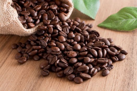 A bunch of coffee beans, falling out of a sack on a wooden background