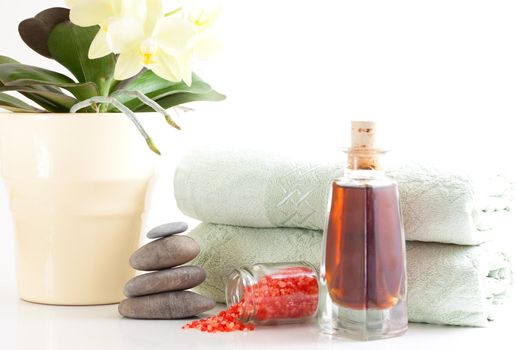 Yellow orchid, massage stones, bath salt, massage oil and two towels isolated on white background