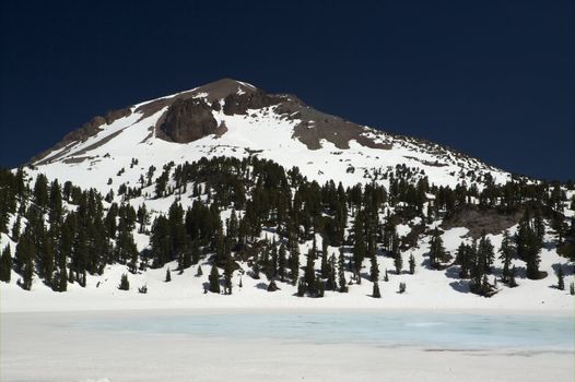 Granite mountain peak  with snow against deep blue sky and frozen blue lake