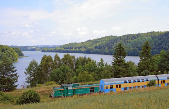 Passenger train passing the village with the river in background
