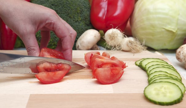 Detail of a knife and hand cutting a tomato.