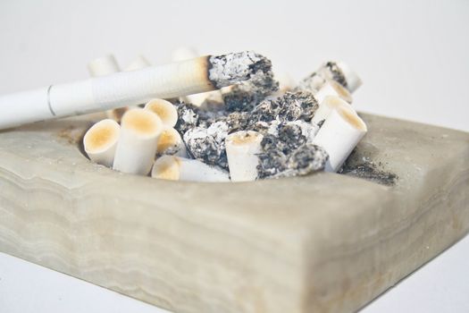 Close-up of a white stone square ashtray full of burnt cigarette butts