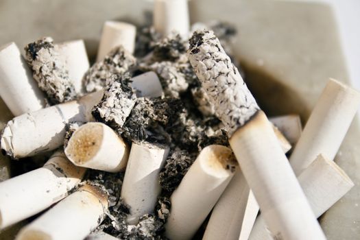 Close-up of a white stone square ashtray that is full of burnt cigarettes