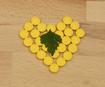 Image of a heart made of yellow pills with a leaf of parsley above it on a chopping board - a health abstract.
