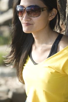 A brunette asian woman wearing a yellow tank top and sunglasses.
