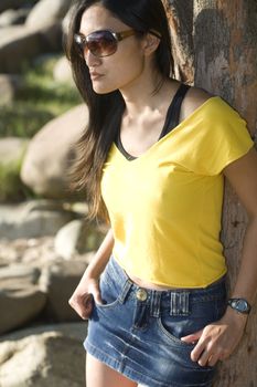 A brunette asian woman wearing a yellow tank top and sunglasses.