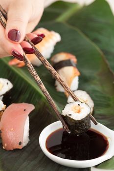 Woman hand with red fingernails holding chopstick to dip a sushi in the soy sauce