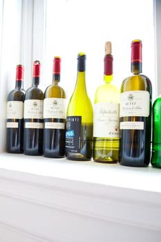Assorted Italian red wine bottles standing on a window shelf.