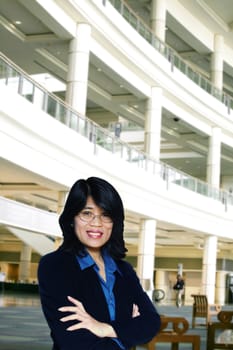 Confident asian business woman standing with arms crossed in large business complex