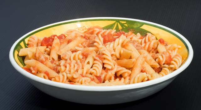 A plate full of italian pasta of two kind (fusilli and penne) over a black background