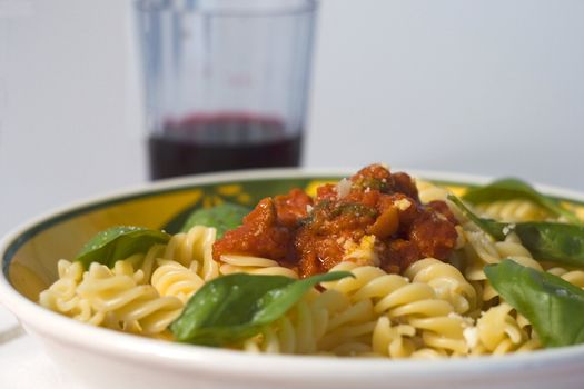 A plate full of italian pasta (fusilli al sugo), over a white background, with a glass of wine on the background