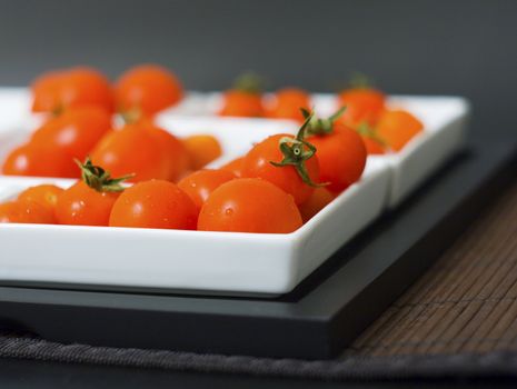 Some little tomatoes in white plates and wooden tablemats
