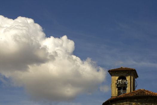 A white cloud in the blue sky, over the belltower of a church