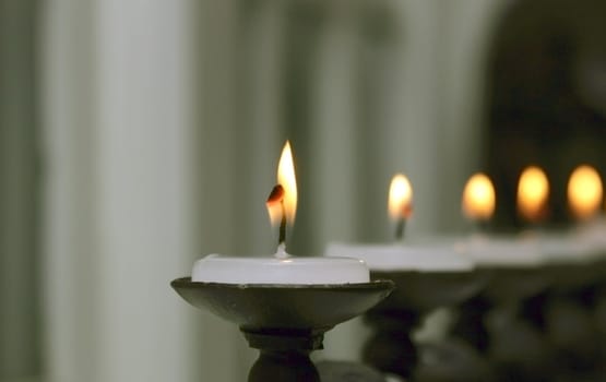 Close up image of a flame from a white candle. Other candles receeding to soft focus in the background.