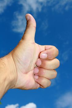 A hand gesture. A hand creating a thumbs up sign, set on a blue sky background