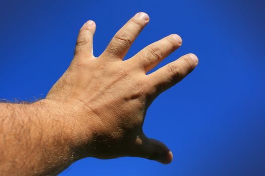 A male hand and forearm poiting skywards with fingers sread out and reaching. Set against a bright blue sky background.