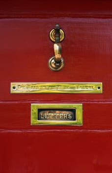 A worn brass letterbox on an old red door, with brass plate and door knocker.