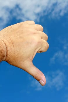 A hand gesture. A male hand making the gesture of thumbs down. Set on a blue sky background.
