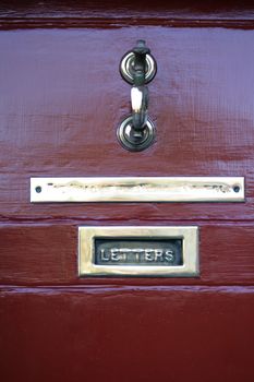 A worn brass letterbox on an old red door, with brass plate and door knocker.