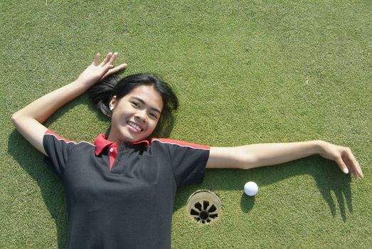 Young, female golf player smiling and embracing the hole at a colf course.